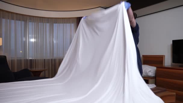 Masked chambermaid covering bed with sheet in room - Footage, Video