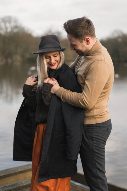 Gentleman covering his girlfriend with a jacket a cold autumn day on a pier - Photo, image