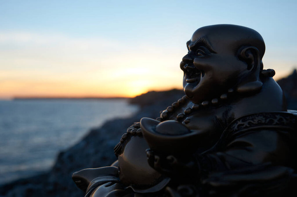 Figura di Buddha, al tramonto, su una scogliera nel mare - Foto, immagini