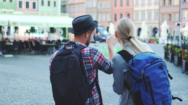 Πίσω όψη του ζεύγους τουριστών με τσάντες έλεγχο χάρτη στην κεντρική πλατεία της πόλης - Φωτογραφία, εικόνα