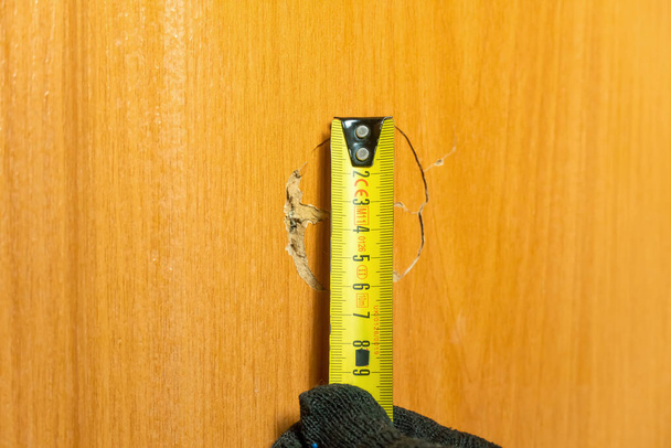 Die Faust durchschlug die Tür und hinterließ ein zerfetztes Loch. Assistent nimmt Messungen vor, um es zu beseitigen. Renovierungskonzept in der Wohnung - Foto, Bild