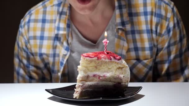 Парень в клетчатой рубашке задувает розовую горящую свечу торта - Кадры, видео