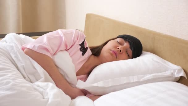 Jeune femme portant un masque de sommeil se trouve détendu dans un lit moderne - Séquence, vidéo