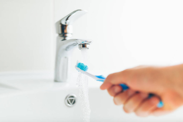 Hand hält Zahnbürste unter fließendem Wasser aus dem Wasserhahn - Foto, Bild