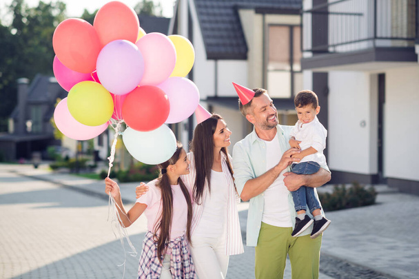 Photo of cheerful family mommy daddy siblings happy smile wear party hat celebrate holiday enjoy weekend air balloons childhood - Foto, imagen