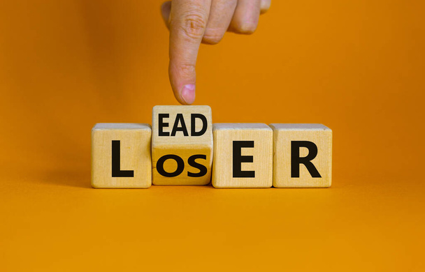 From loser to leader symbol. Businessman turns a wooden cube and changes the word 'loser' to 'leader' or vice versa. Beautiful orange background, copy space. Business and loser or leader concept. - Foto, immagini