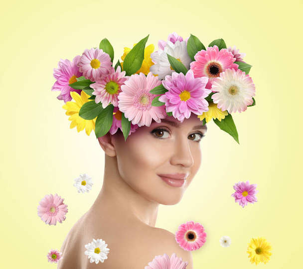 Pretty woman wearing beautiful wreath made of flowers on light yellow background - Foto, Bild