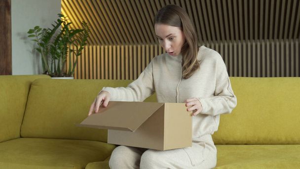 Smiling woman sit on sofa at home open cardboard delivery package shopping online - Foto, Bild