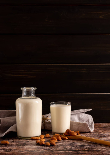 Γάλα αμυγδάλου σε μπουκάλι και ποτήρι, σε σκούρο vintage ξύλινο φόντο, με copy-space - Φωτογραφία, εικόνα
