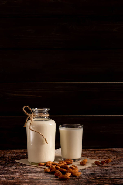 Мигдальне молоко в пляшці і склянці, на темному вінтажному дерев'яному фоні, з копіювальним простором
 - Фото, зображення