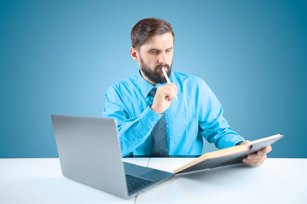 солидный человек в офисе за столом записывает финансовые операции в блокнот - Фото, изображение