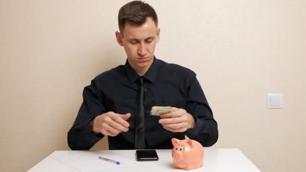 Молодой человек держит долларовые банкноты, выписывая семейные расходы - Кадры, видео