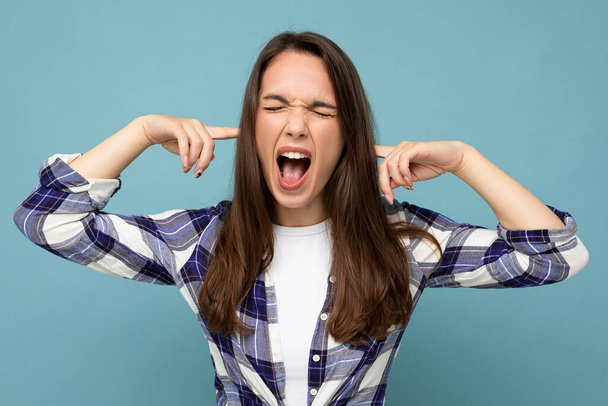 Dont want to hear it Young emotional attractive brunette female person isolated on blue background with copy space and covering ears and shouting - Photo, Image