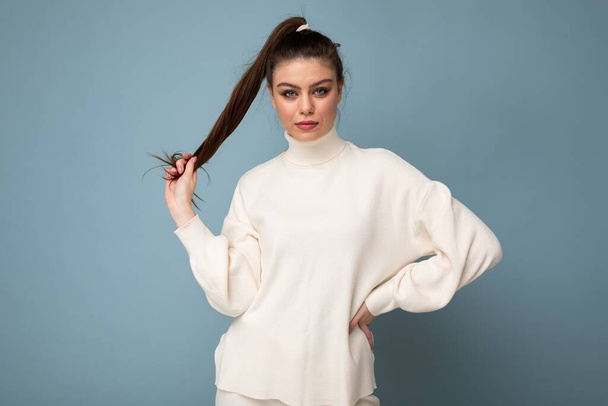 młody fascynujące biały moda brunetka kobieta noszenie casual biały sweter ustawienie odizolowany na niebieski tło ściana - Zdjęcie, obraz