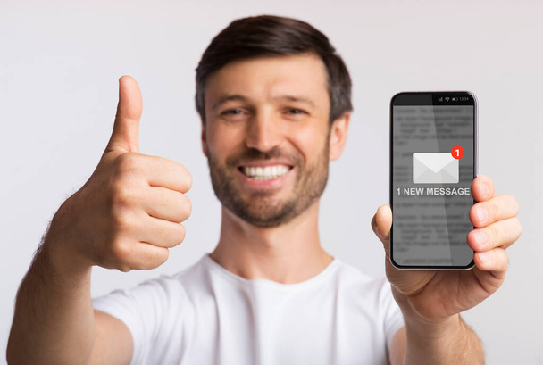 Mies näyttää älypuhelimen, jossa on uusi viesti Gesturing Thumbs-Up, harmaa tausta - Valokuva, kuva