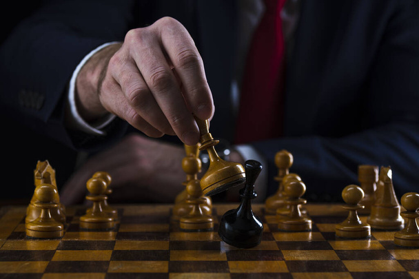 concept of strategy and business planning, businessman behind a chessboard white queen beats a black chess piece, strategy and tactics, readiness for battle, start of battle. - Foto, afbeelding