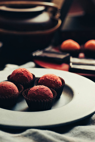 Vier Bonbons auf einem grauen Teller. Teekanne und Schokolade als Hintergrund - Foto, Bild