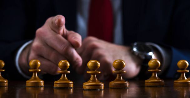 koncepcja strategii i planowania biznesowego, biznesmen przy szachownicy przed ustawionymi białymi pionkami daje wskazówkę do przodu, strategia i taktyka, gotowość do walki, początek bitwy. - Zdjęcie, obraz