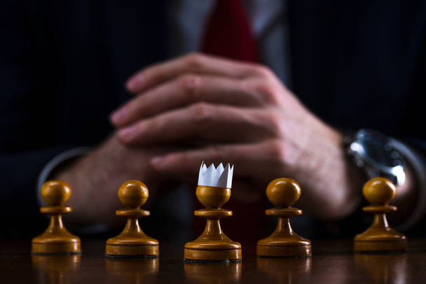 the concept of strategy and business planning, a businessman at a chessboard in front of lined up white pawns, one of which is in a paper crown, strategy and tactics, readiness for battle, the beginning of the battle. - Foto, Bild