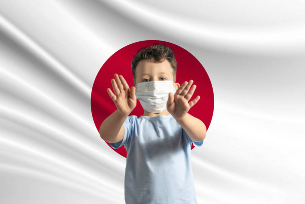 Pieni valkoinen poika suojelevassa naamiossa Japanin lipun taustalla tekee stop-merkin käsillään, jää kotiin Japani. - Valokuva, kuva