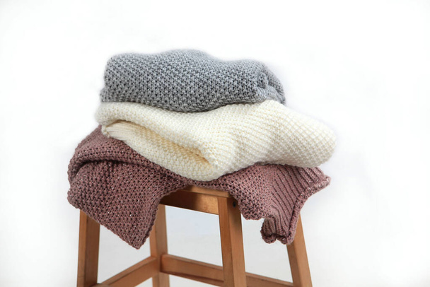 Knitted woolen clothes lie on a wooden chair. Clothes made of natural wool for the cold season. Sweaters with chunky knits. Light background. No people. - Foto, afbeelding