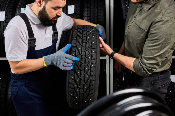 mécanicien caucasien tenant un pneu et montrant des pneus de roue au service de réparation automobile et magasin d'automobiles - Photo, image