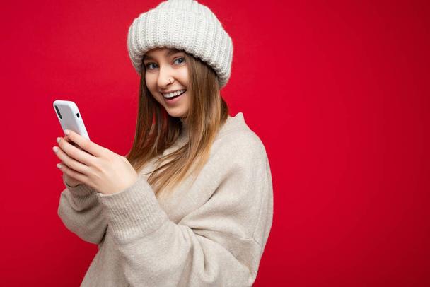Zdjęcie atrakcyjnego pozytywnego wyglądu młodej kobiety ubranej w stylowy strój, odizolowanej na tle z pustą przestrzenią trzymającą w dłoni i korzystającej z sms-ów z telefonu komórkowego patrzących na - Zdjęcie, obraz