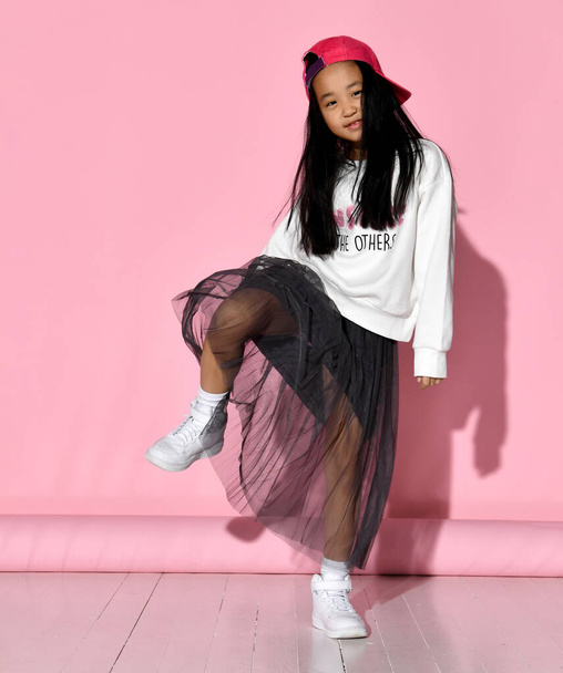 Side view of a little Korean girl model posing in the studio on a pink background raising her leg. - Фото, зображення