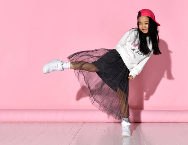 Side view of a little Korean girl model posing in the studio on a pink background raising her leg. - Foto, Bild