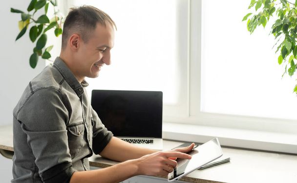 Uśmiechnięty młody człowiek freelancer za pomocą laptopa, nauka online, praca w domu, szczęśliwy przypadkowy facet pisząc na komputerze notebook surfing internet, korzystając z odległej pracy, siedzieć przy stole. - Zdjęcie, obraz