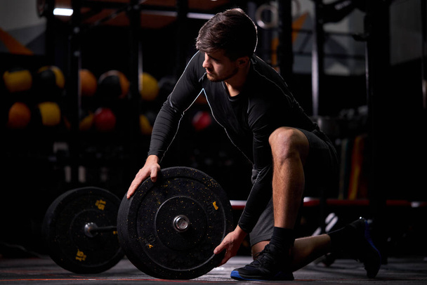 Young sportsman powerlifter preparing for deadlift of barbell during competition - 写真・画像