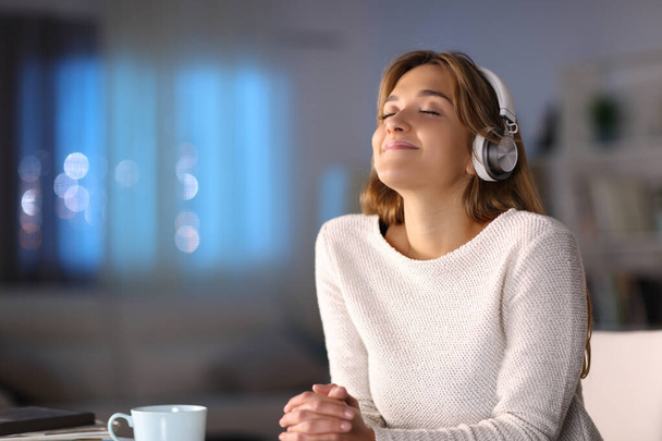 Woman wearing wireless headphones relaxing listening to music at home in the night - 写真・画像