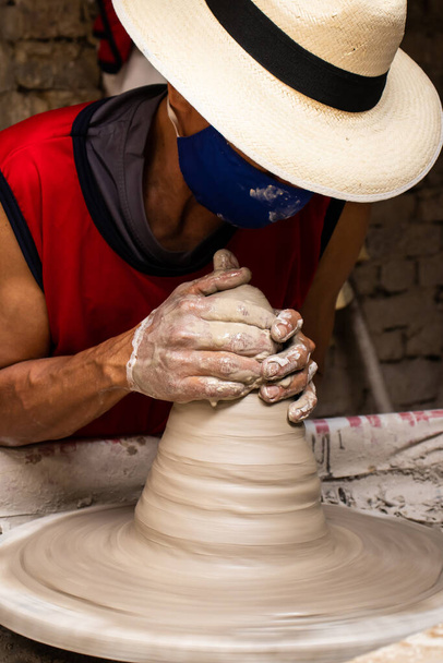 Az ember kerámiatermékeket készít a kerámiakerekeken egy hagyományos gyárban Raquira városában, amely Kolumbia Cundinamarca megyéjében található. - Fotó, kép