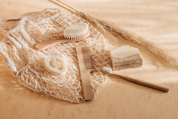 Zero Waste Badezimmeraccessoires Haarbürste, Bambus-Zahnbürste, Luffa und Naturseife in wiederverwendbarer Einkaufstasche auf beigem Hintergrund. Ansicht von oben. Vintage-Farbfilter - Foto, Bild