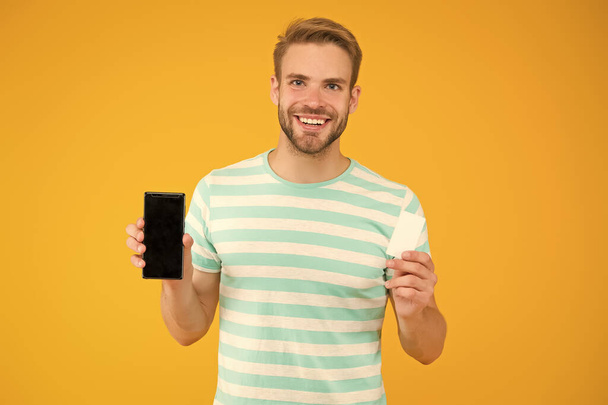 On sale for less. Happy man hold gift card and smartphone. Mobile phone deal for sale. Special offer. Sale price. Super sale in shop and online. Go shopping. Buy now and get discount card, copy space - Fotoğraf, Görsel