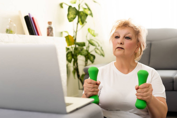 Formazione interna. Donna anziana attiva che fa esercizio davanti al computer portatile a casa, spazio libero - Foto, immagini