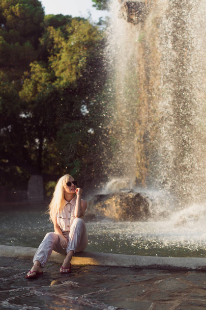美しい若い女性が滝の背景に座っています - 写真・画像