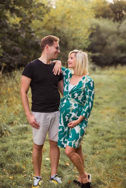 The smiling pregnant couple is standing in the garden and looking at each other - Fotografie, Obrázek