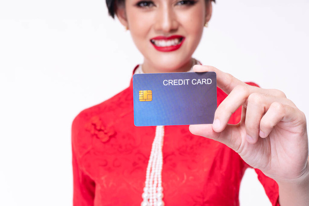 Zuversicht für ein Zahlungskonzept. Hand einer jungen Frau trägt rotes chinesisches Cheongsam-Kleid mit Kreditkartenattrappe, während sie vor isoliertem weißem Hintergrund steht. - Foto, Bild