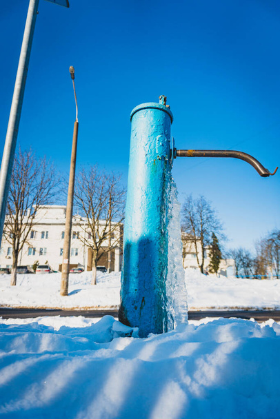 Water bevroor op de drinkwaterkolom, blauwe waterpomp bedekt met ijs, ijs uit de waterput - Foto, afbeelding