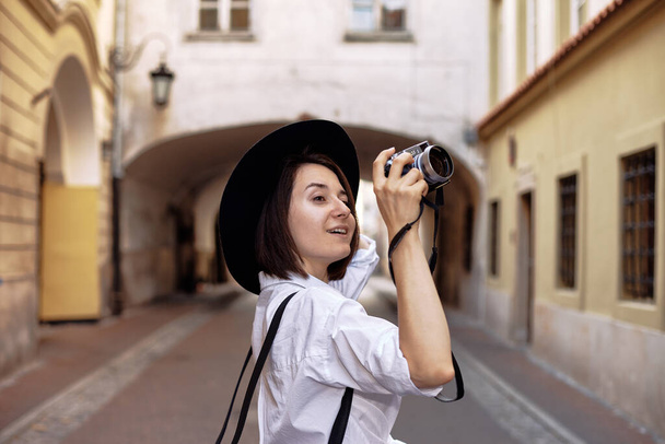 Dziewczyna w czarnym kapeluszu strzelająca w starym europejskim miasteczku. - Zdjęcie, obraz