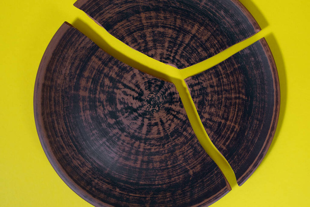 Rozbitý hliněný talíř s krásným vzorem na žlutém pozadí. Volné místo pro text. Keramika je rozdělena do tří částí. Rozbité vztahy nebo sny - Fotografie, Obrázek