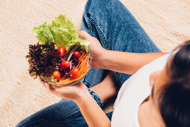 Top view of female hands holding bowl with green lettuce salad on legs, a young woman eating fresh salad meal vegetarian spinach in a bowl, Clean detox healthy food concept - 写真・画像