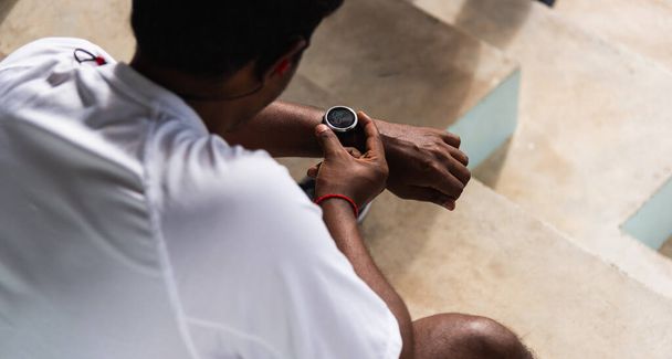 Close up Asian young athlete sport runner black man wear modern time smart watch he sitting resting before training running at the outdoor street health park, healthy exercise before workout concept - 写真・画像