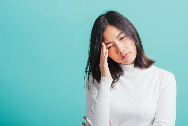 Young beautiful Asian woman holding her hands to her temples with a severe headache, Portrait sad female unhappy suffering from migraine, studio shot isolated on a blue background - Foto, imagen