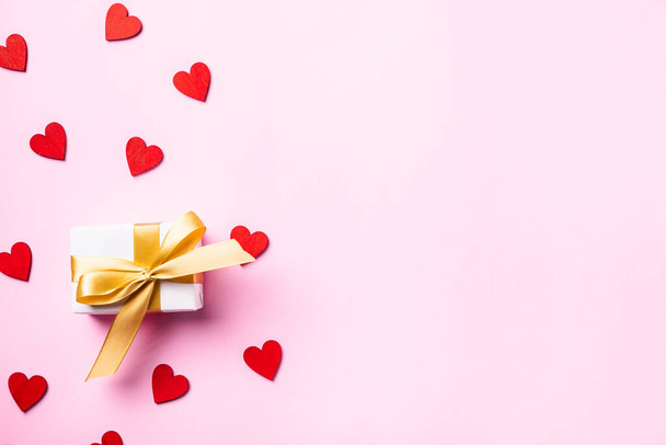 Happy Valentines' day background concept. White gift box with a golden bow ribbon and wood red hearts composition for love isolated on pink background with copy space. Top View from above - Φωτογραφία, εικόνα