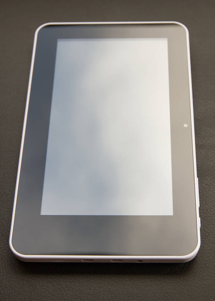 Tableta digital posada superficie de cuero negro que refleja el cielo con nubes - Foto, imagen