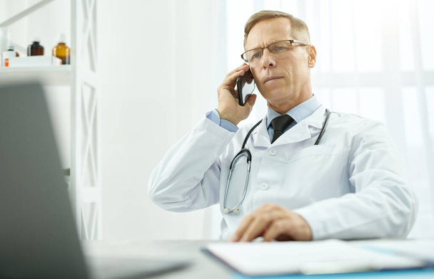 Przystojny lekarz rozmawiający przez telefon w klinice - Zdjęcie, obraz