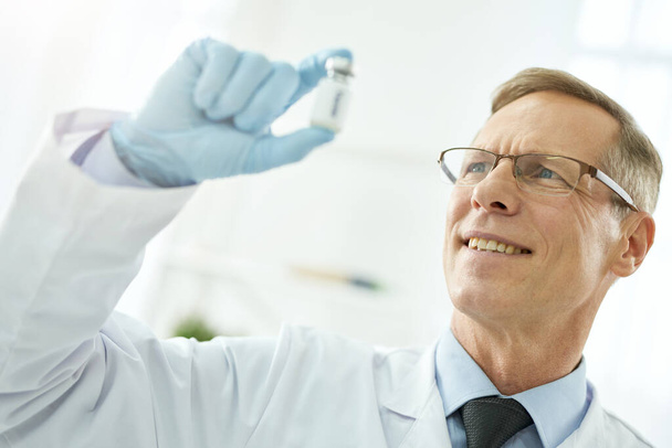 Vidám férfi orvos szemüveg kezében üveg vakcina - Fotó, kép