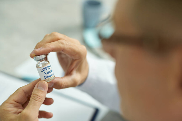 Erkek eli, elinde bir şişe covid-19 aşısı tutuyor. - Fotoğraf, Görsel